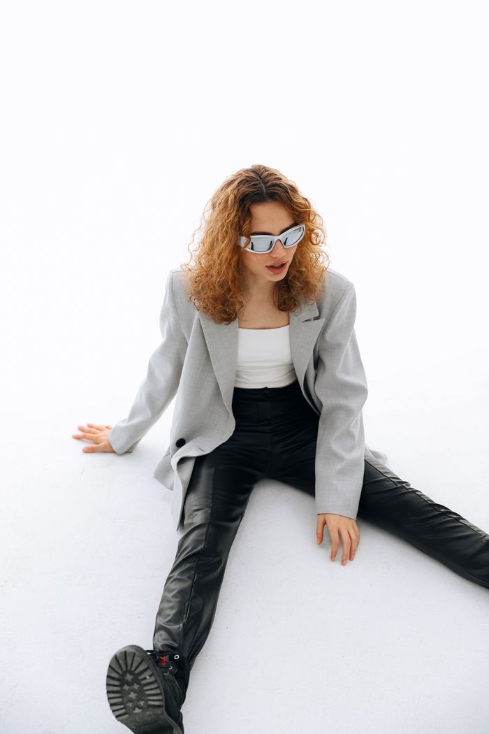 gallery-04 Woman in trendy outfit sitting on white floor, wearing edgy sunglasses for fashion look.