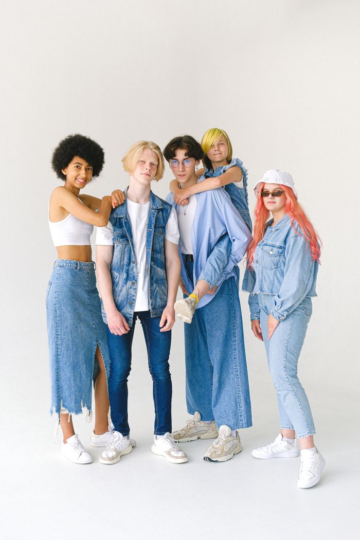 Full body group of smiling teenage friends in jeans clothes standing against white background and looking at camera