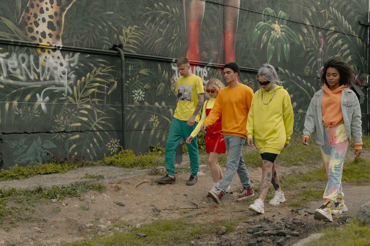 home-img A group of trendy young adults walking by a vibrant urban mural, showcasing street style fashion.