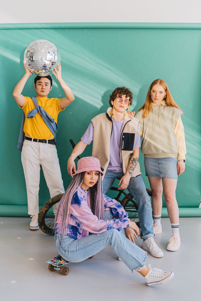 Diverse group of young adults posing with a disco ball against a green backdrop.