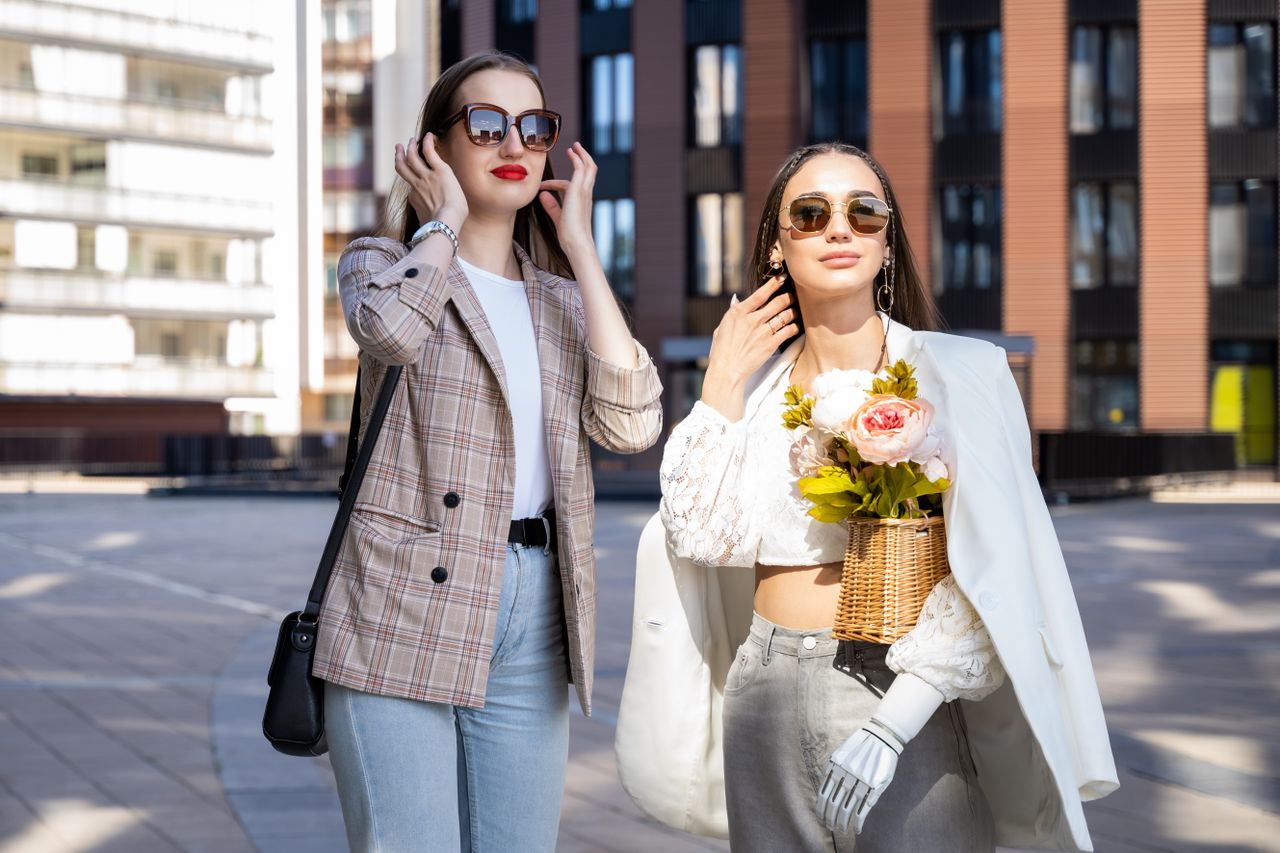 gallery-01 Two stylish women enjoy a sunny day in the city wearing chic outfits and sunglasses.